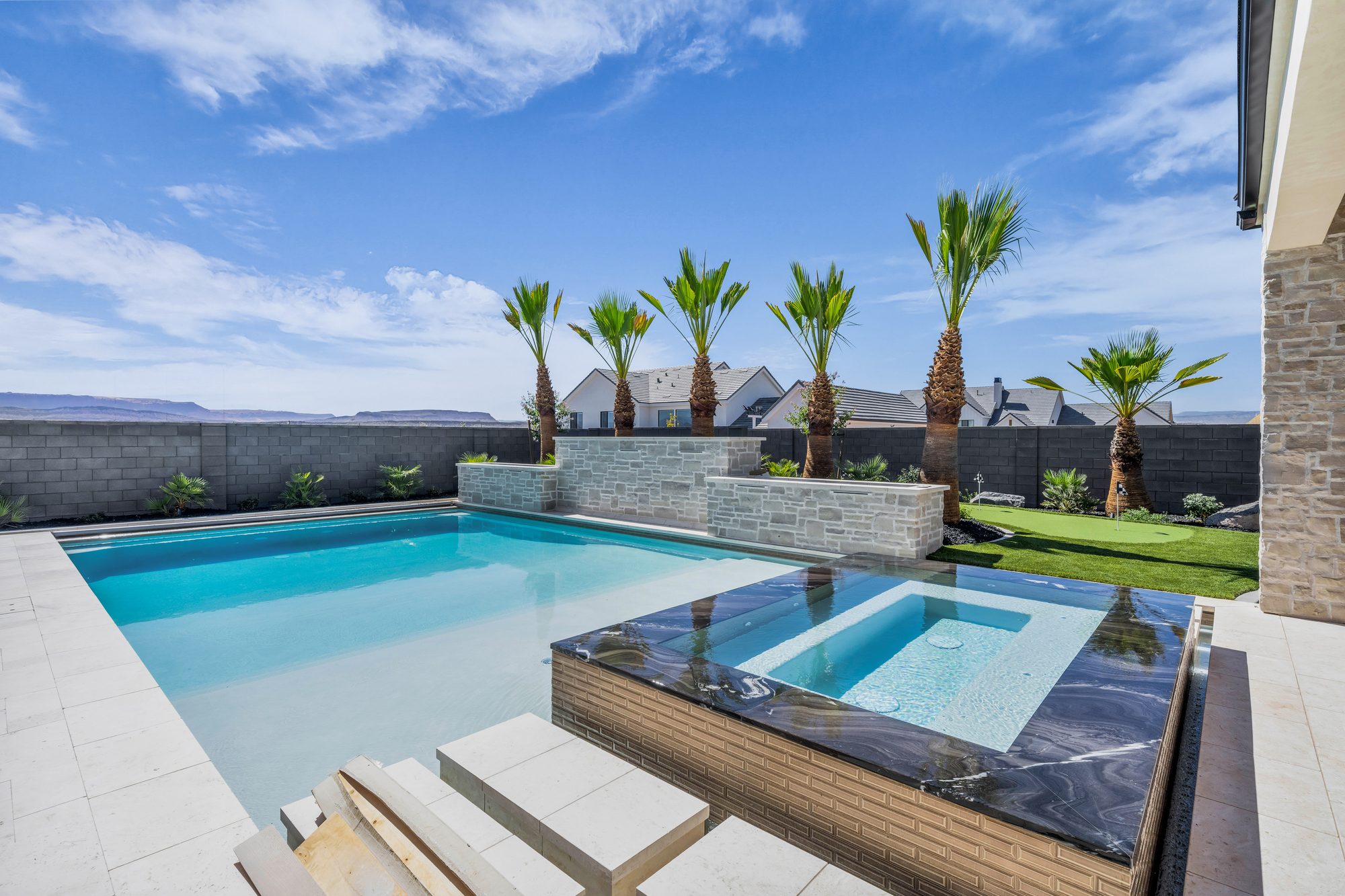 Raised spa with stone veneer spilling into a custom pool, built by Paragon Pools in St. George, Utah
